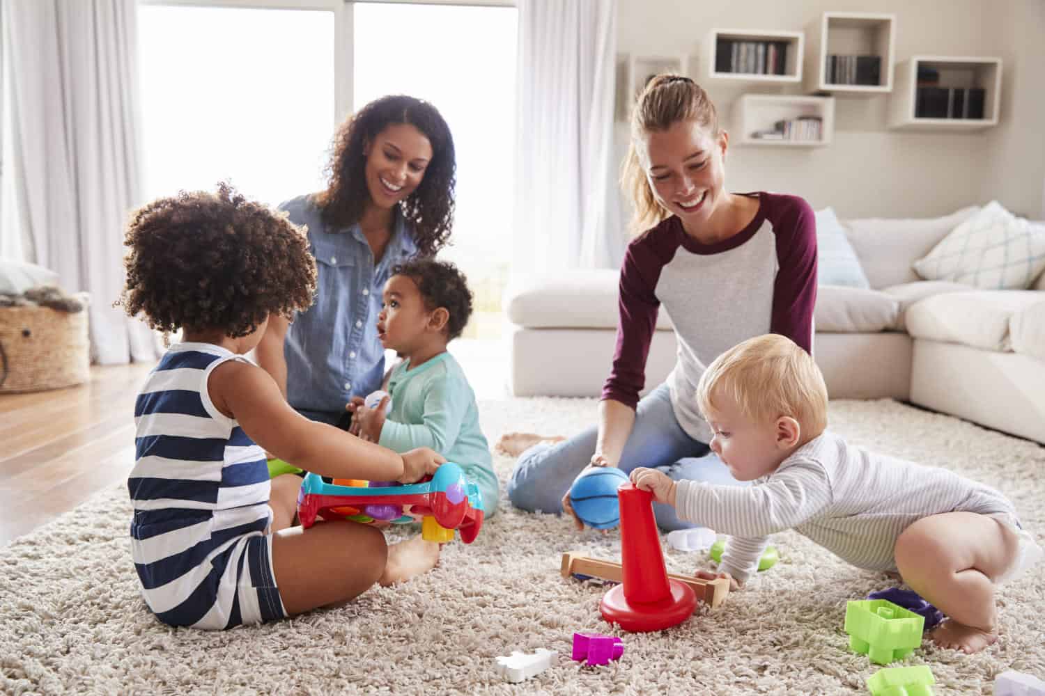 Photo of two friends playing with toddler kids on sitting room floor